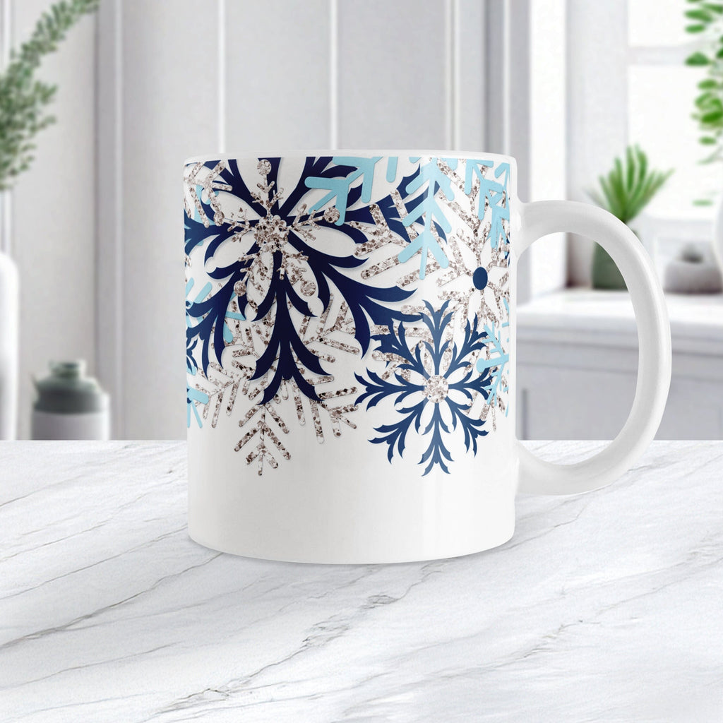 Winter Blue Silver Snowflake Mug (11oz) at Amy's Coffee Mugs. A ceramic coffee mug with navy blue, aqua blue, and silver-colored glitter-illustrated snowflakes along the top, cascading down most of the mug, over white. This wintry snowflake design wraps around the mug up to the handle. Image shows the mug on a white marble countertop.